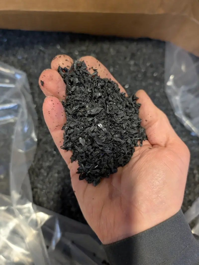 A handful of black plastic regrind over an open box