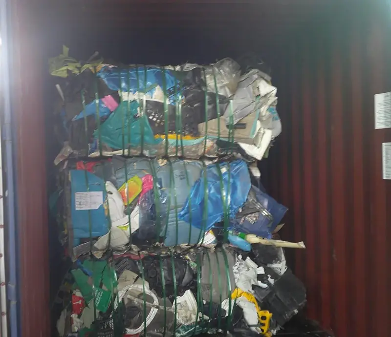 Strapped bales of mixed rigid plastic inside a red shipping container
