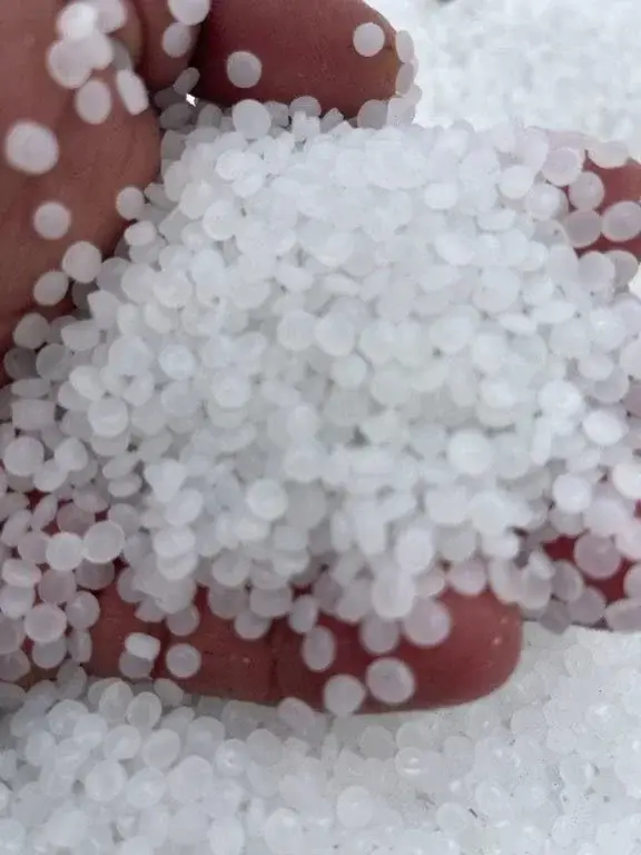 A hand holding white PE resin pellets